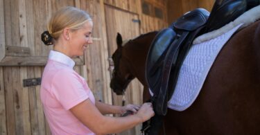 woman tightening girth on horse