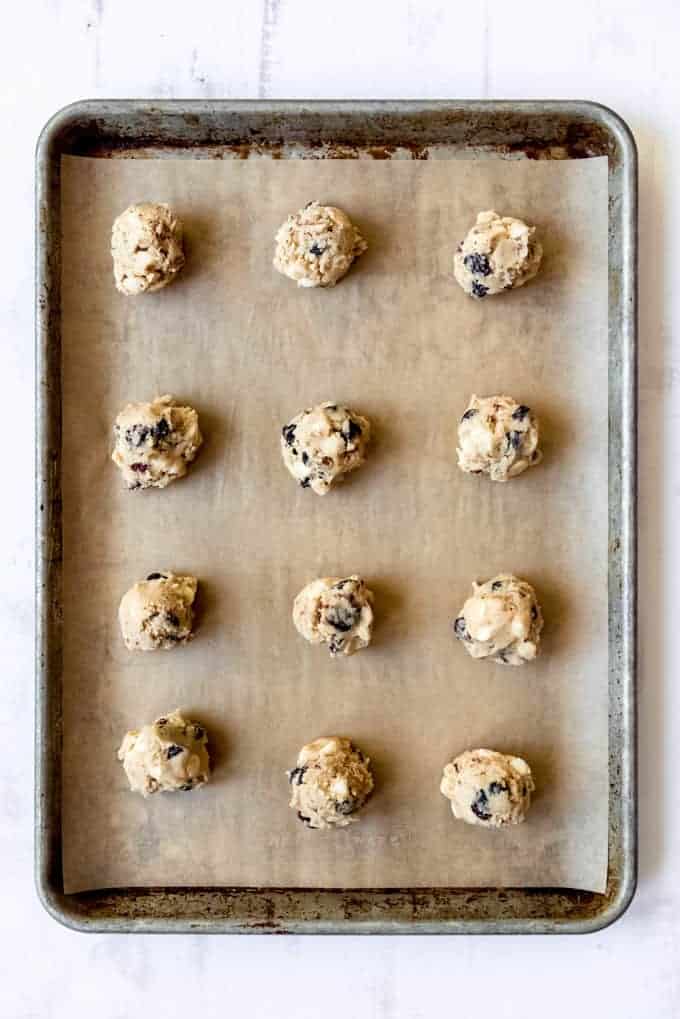 Balls of cookie dough are evenly spaced on a cookie sheet lined with parchment paper, ready to be placed in the oven. 