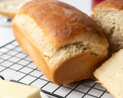 A loaf of fresh homemade Amish white bread on a cooling rack in front of a butter plate with softened butter.