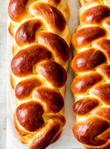 Two loaves of braided challah bread on parchment paper.