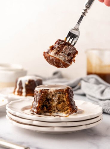 An image of a fork holding a bite of sticky toffee pudding over the rest of the cake on dessert plates.