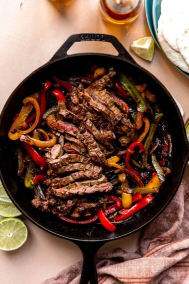 Large cast iron skillet filled with sliced grilled steak and grilled bell peppers and onions.