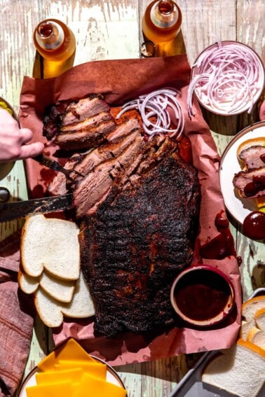 Texas Brisket on peach paper, sliced with slices of bread, cheese, pickles and onions around.