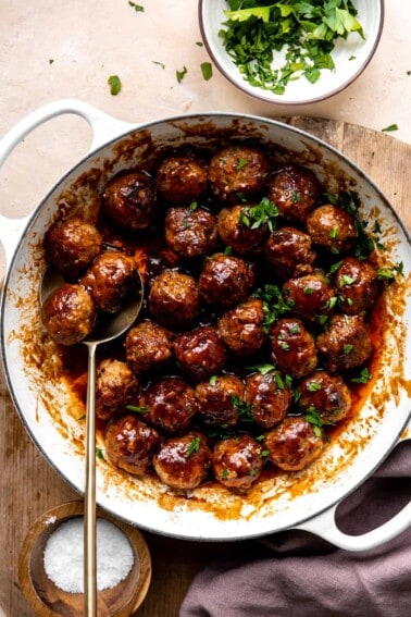 White skillet filled with bacon bourbon meatballs and topped with fresh parsley.