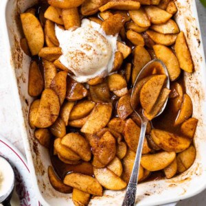 Baking dish filled with baked apples swimming in a cinnamon spiced syrup and topped with vanilla ice cream.