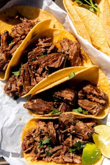 Shredded Beef tacos laid out on the counter in the sun with lime wedges and fresh cilantro.