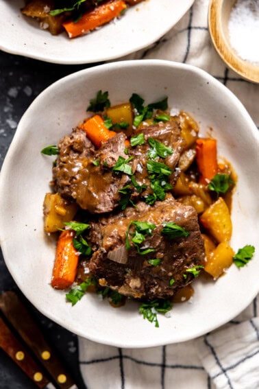 Bowl with pot roast, carrots, and potatoes all garnished with fresh parsley.