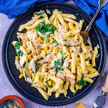 Leftover chicken pasta on a black plate.