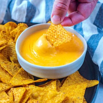 A tortilla chip being dipped into some nacho cheese sauce.