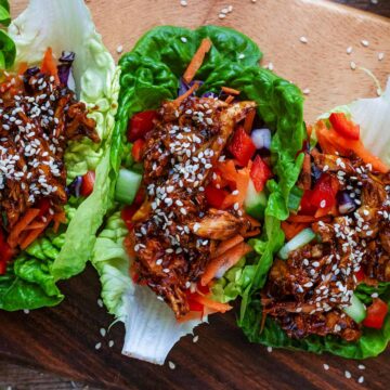 Three teriyaki chicken lettuce wraps on a wooden board.