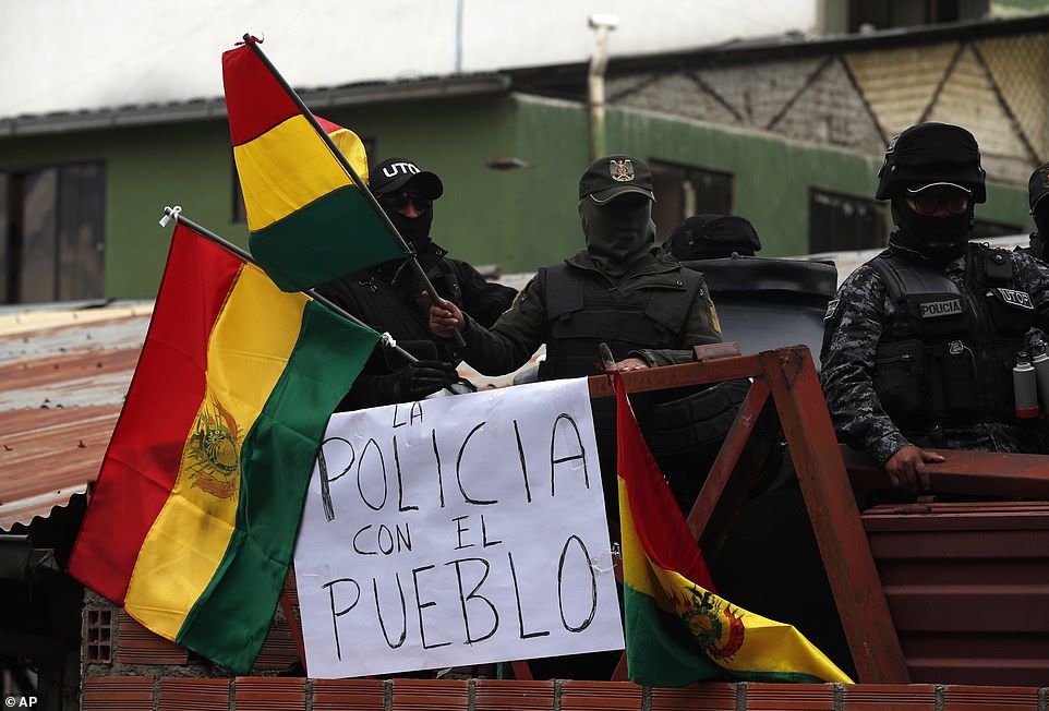 Police against the reelection of President Evo Morales stand on the rooftop of a police station waving national flags near a sign with a message that reads in Spanish: 'The police is with the people', just meters away from the presidential palace, in La Paz, Bolivia, today