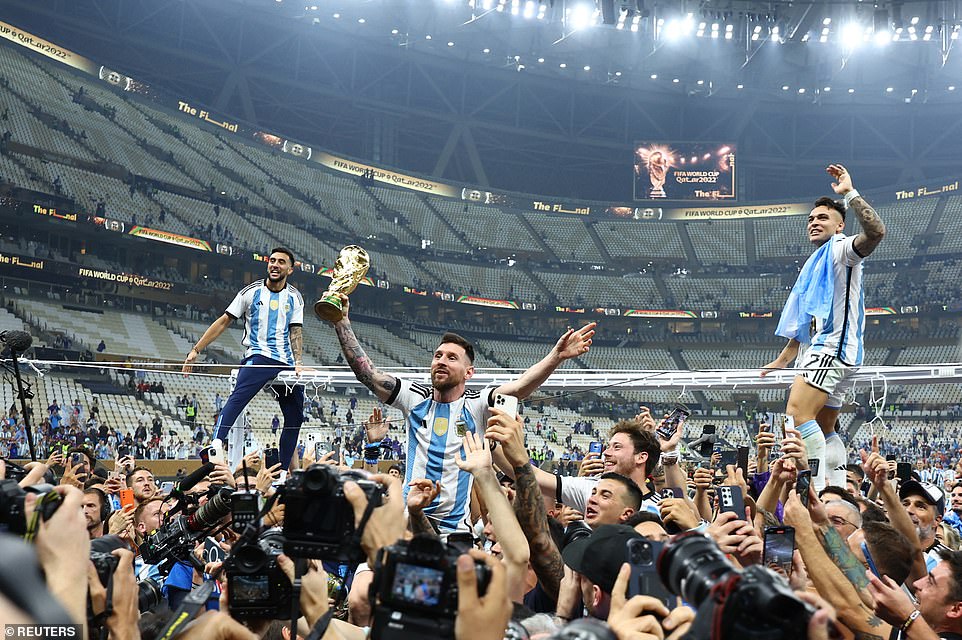 Argentina's Lionel Messi celebrates with the trophy and fans after winning the World Cup as Lautaro Martinez sits atop the frame of the goal