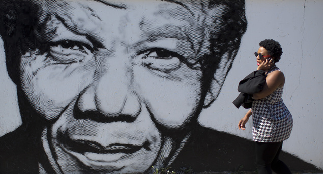 A South African woman talks on her mobile phone as she walks past a mural depicting the late former South African President Nelson Mandela, in the Soweto tow...