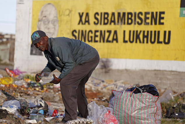 A man collects plastic bottles to make money, in front of a painted Election poster showing the face of South African President Jacob Zuma, on a wall in Nyan...