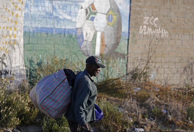 A man that make a living by picking up plastic bottles walk past a graffiti image of a soccer ball, painted onto a wall in Nyanga township on the outskirts o...