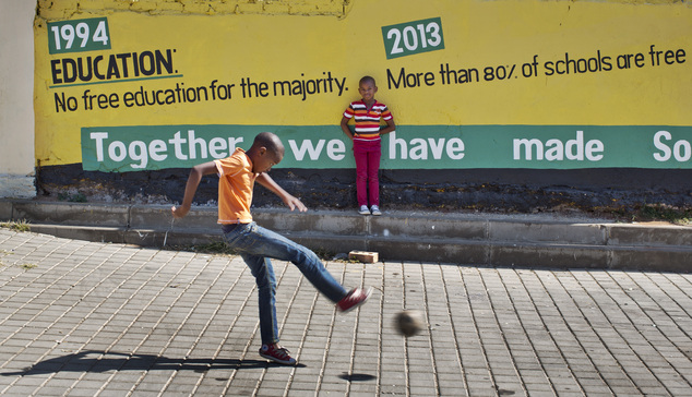 Children play football in front of a mural of the African National Congress (ANC) proclaiming their achievements over the last 20 years, in the Soweto townsh...