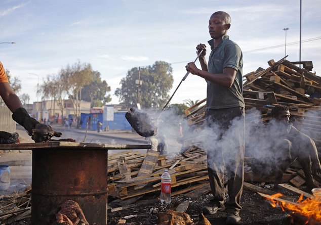 A cook holds a sheep's head in a fire to barbeque it to sell to customers at a local market in Nyanga township on the outskirts of the city of Cape Town, Sou...