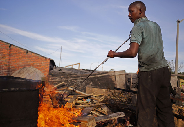 A cook holds a sheep's head in a fire to barbeque it to sell to customers at a local market in Nyanga township on the outskirts of the city of Cape Town, Sou...