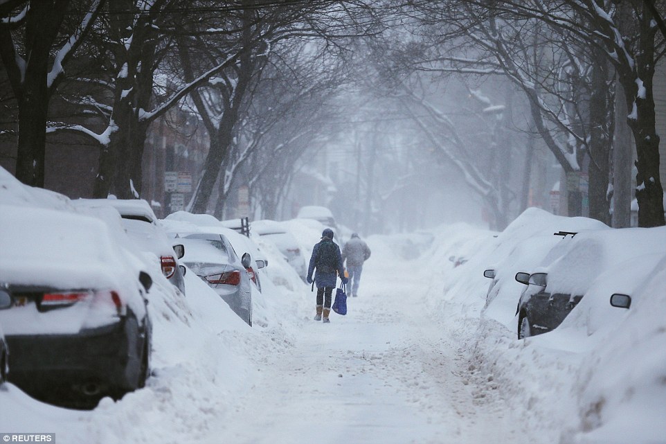 Covered: Pedestrians make their way along a snow-covered street in Cambridge, Massachusetts on Monday as the area is battered with yet another snowstorm, which is expected to last through Tuesday. The area could get as many as two feet of snow