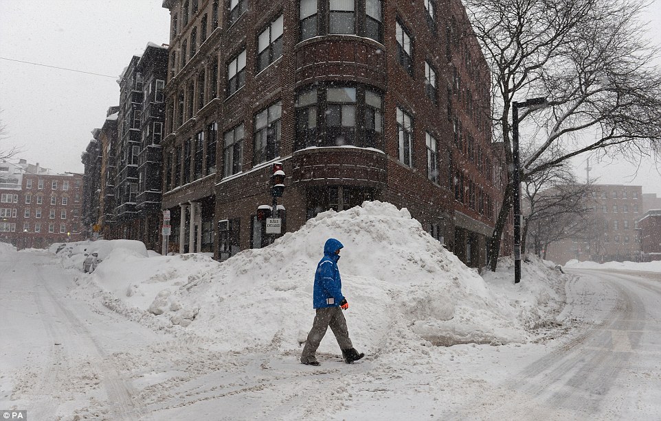 Piling up: A man walks past mounds of snow on a block in Boston on Monday as the city struggles to remove it quick enough