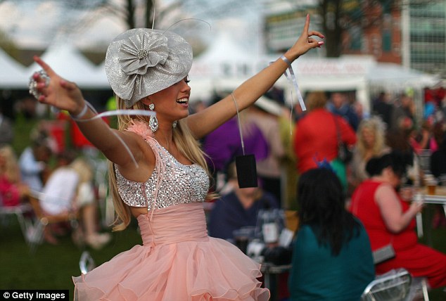 A woman in a bedazzled dress dances with her arms in the air at the Aintree Grand National meeting in 2012 