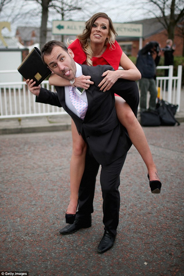 A man awkwardly gives a woman a piggyback ride as racegoers make their way home from  Ladies' Day