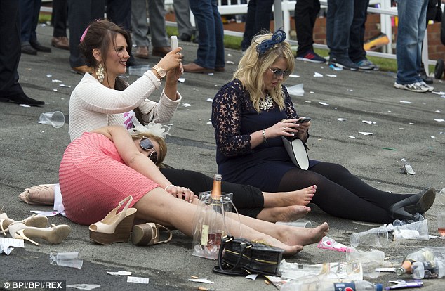 A female racegoer slumps over her friend on the ground surrounded by rubbish