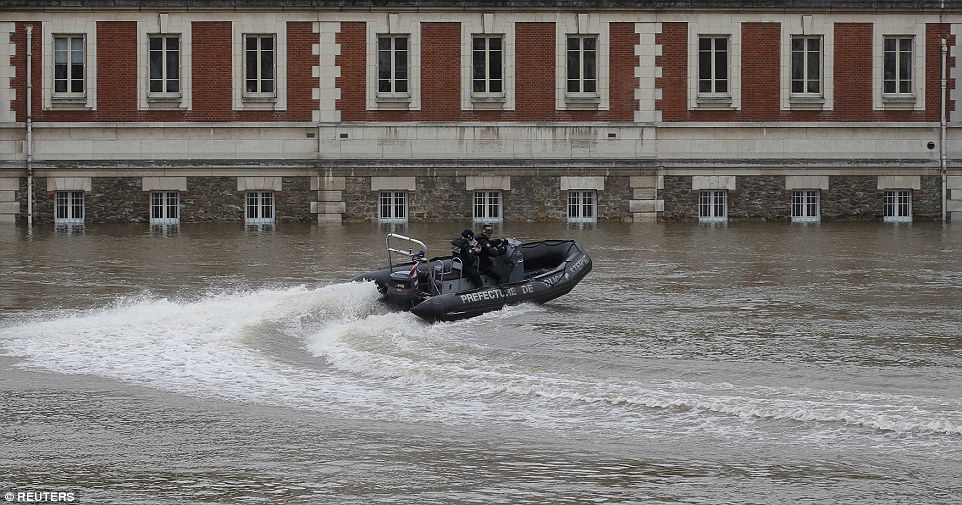 French police officers on a rescue boat patrol past a flooded building on the edge of the Seine River, near Notre-Dame Cathedral