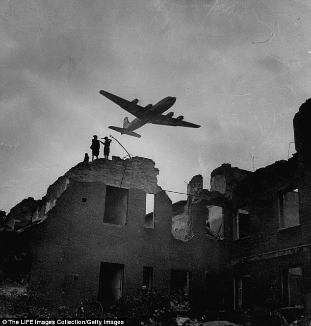 Children play on the roofs of the destroyed buildings as relief planes fly overhead 