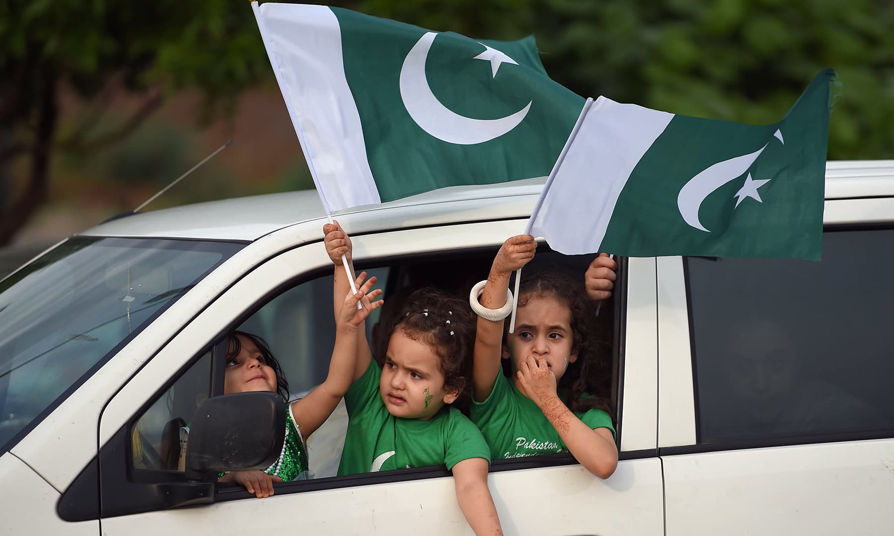 Children wave national flags from a car as they take part in Independence Day celebrations in Islamabad.— AFP