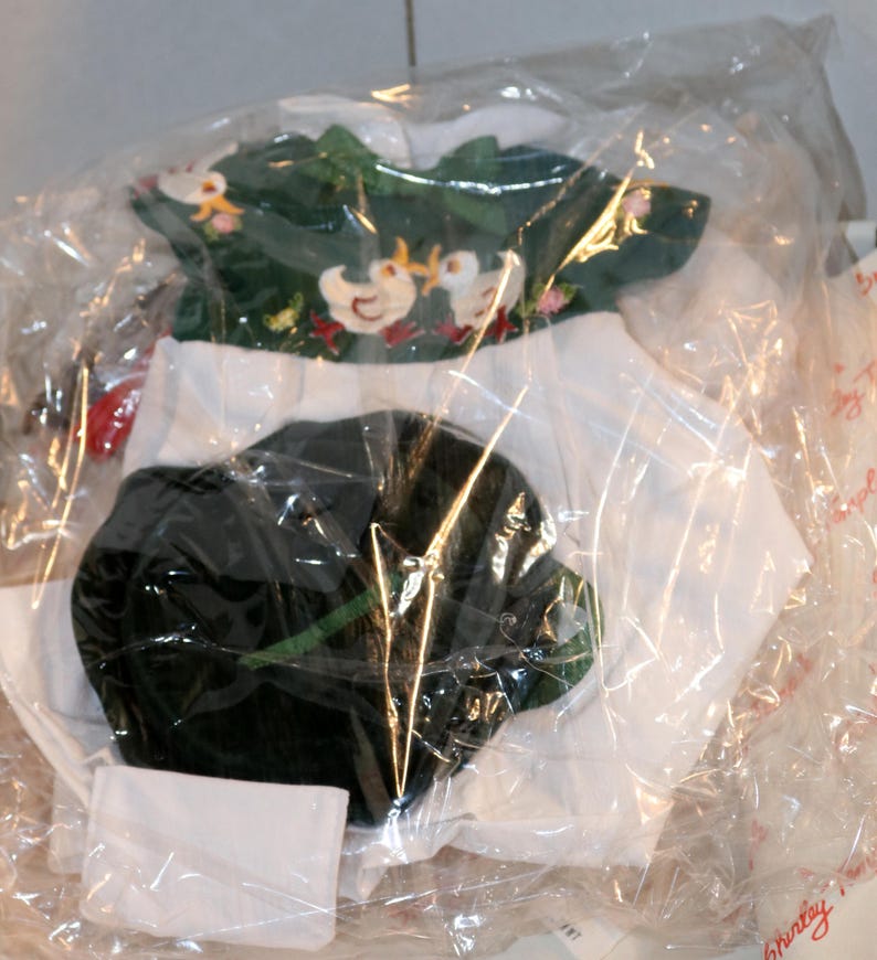 May include: A green and white doll outfit with a green hat. The outfit is made of a soft fabric and has a simple design. The outfit is packaged in a clear plastic bag.