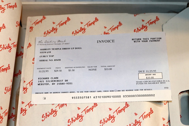 May include: An invoice from the Danbury Mint for a Shirley Temple dress up doll. The invoice is dated 11/21/95 and the total amount due is $33.00. The invoice is addressed to Richard Clark at 1021 Silvercrest Dr, Webster, NY 14580-9351. The invoice includes the item number, description, price, shipping and handling, sales tax, and total amount. The invoice also includes a due date of 11/25/95 and instructions for making payments.