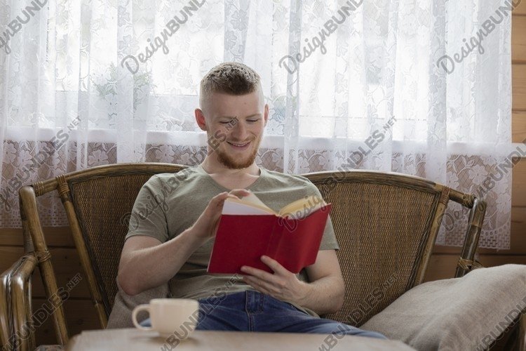 young man reading book with red cover on wicker bench example image 1