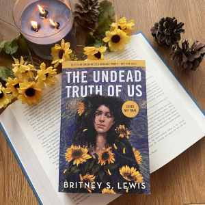 The book on a wooden background surrounded by yellow flowers, pine cones and a blue candle