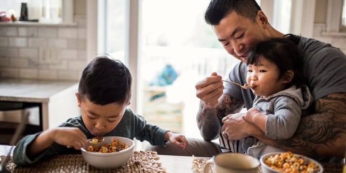 Father with a conforming mortgage feeding his two small children cereal at the breakfast table.