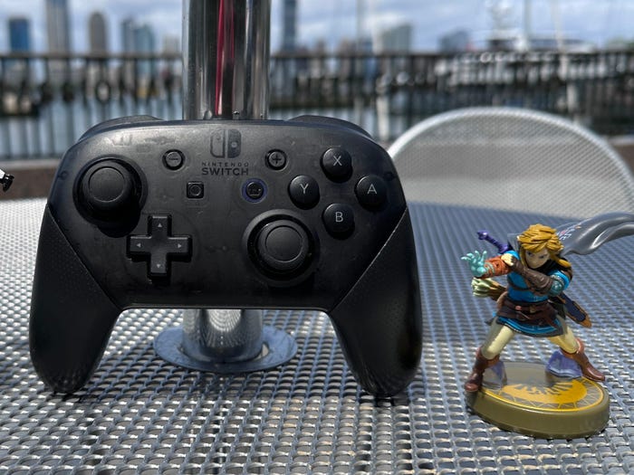 A Nintendo Switch Pro Controller and two Nintendo Amiibo figures set against a city skyline.