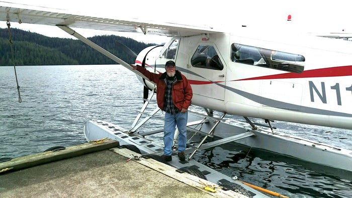 A pilot stands in front of a small aircraft in the water.