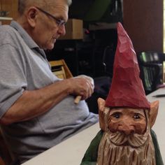 an older man sitting at a table with a gnome figurine next to him