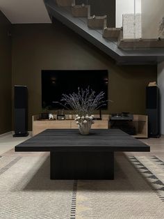 a living room with a black coffee table in the center and stairs leading up to it