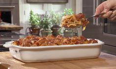 a person is spooning some food out of a casserole dish in the kitchen