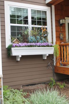 a wooden porch with flowers and plants in the window box on the side of the house