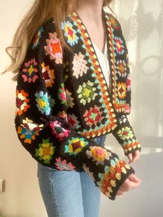 a woman is wearing a colorful crocheted jacket and jeans with her hands in her pockets