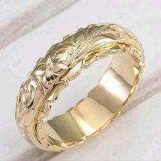 a gold wedding band with flowers and leaves in the center on a white tablecloth