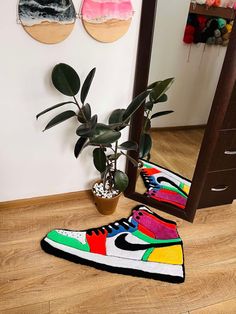 a pair of sneakers sitting on top of a wooden floor next to a potted plant