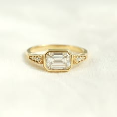 a yellow gold ring with an emerald stone and two diamonds on the band, sitting on a white surface