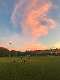 two people standing on top of a lush green field under a pink and blue sky