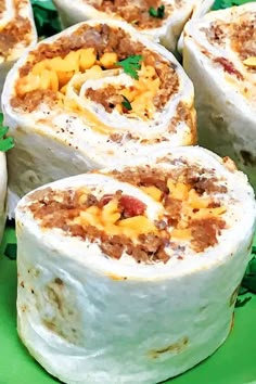 several burritos are arranged on a green platter and garnished with cheese