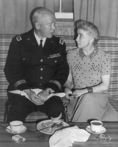 an old black and white photo of a man in uniform talking to a woman sitting on a couch