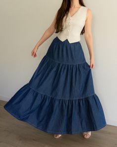 a woman in a long blue skirt standing against a wall