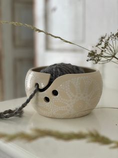 a cat is sitting in a bowl on the table next to some flowers and yarn